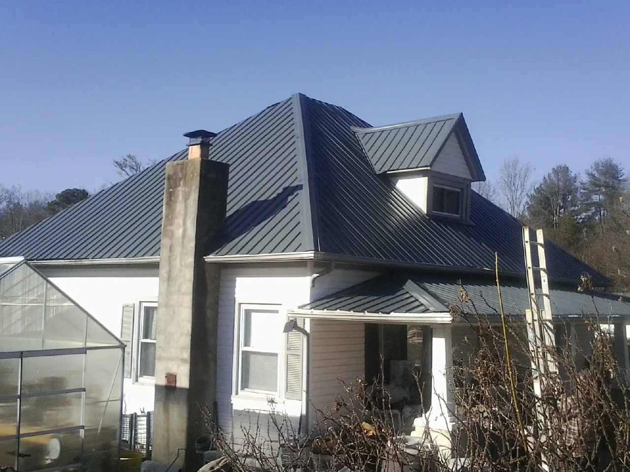 Dark blue standing seam metal roof on a white farmhouse with dormer — Slate & Tile Roof Repair by Roofing Brothers in Staatsburg