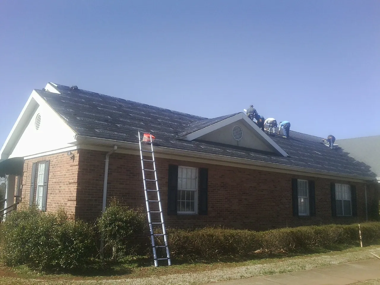 Crew tearing shingles off a brick ranch roof with a ladder set — Metal Roof Repair work by our crew in Staatsburg
