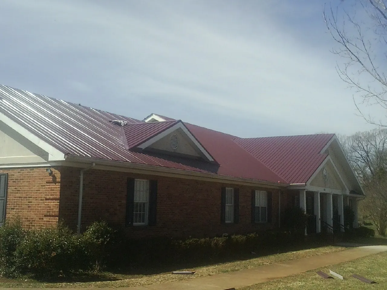 Red metal roof with gabled entries on a long brick building, from a Hail Damage Roof Repair job in Staatsburg