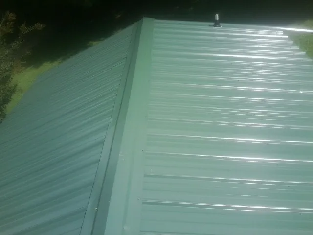 New green metal panels meeting at the ridge of a roof — Flat Roof Repair work by our crew in Staatsburg