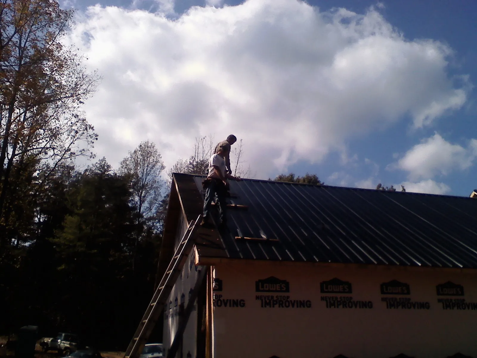 Roofer fastening dark metal panels high against a cloudy sky, from a Roof Inspection job in Staatsburg