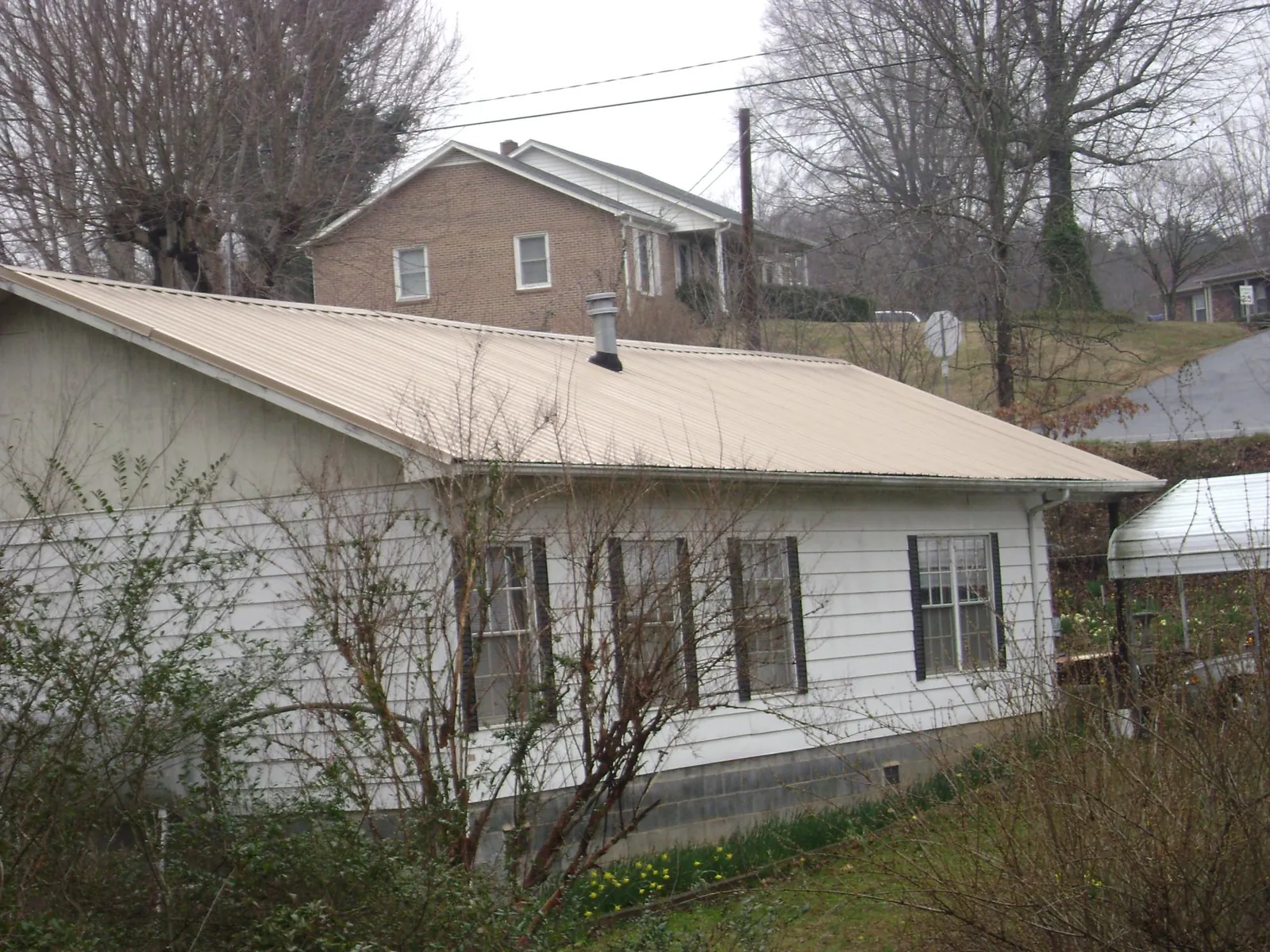 Tan metal roof on a white sided house set into a hillside — Commercial Roofing by Roofing Brothers in Staatsburg