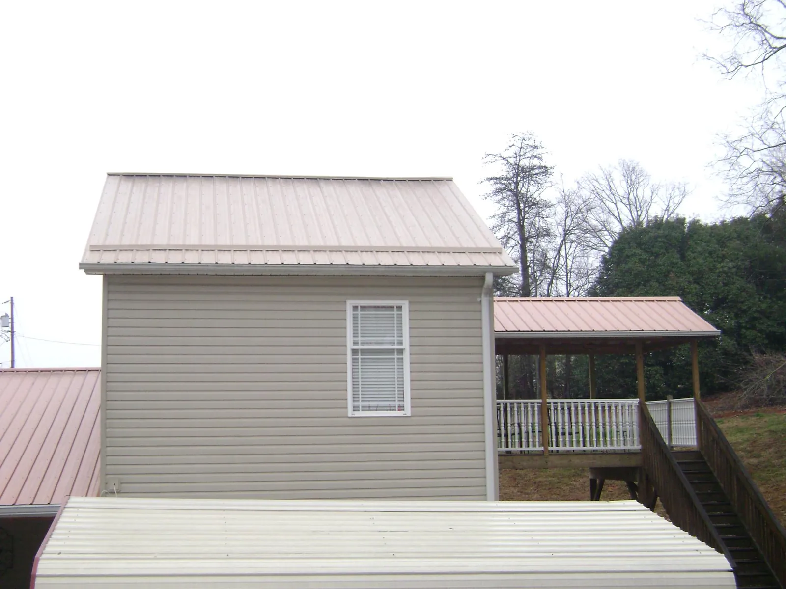 Tan metal roofs on a two story addition and attached porch, from a Roof Replacement job in Staatsburg